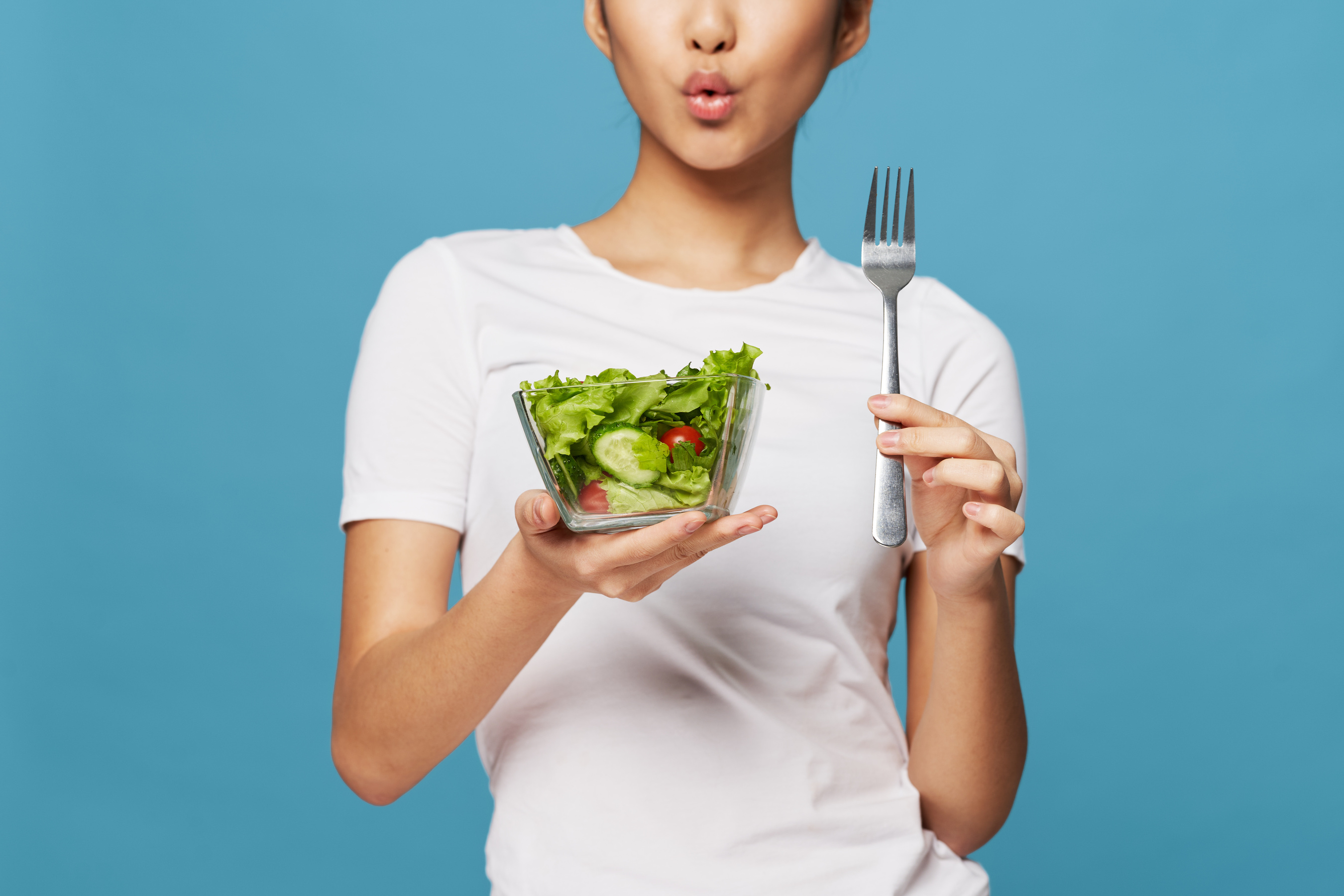 a person holding a fork with a salad in front of them.